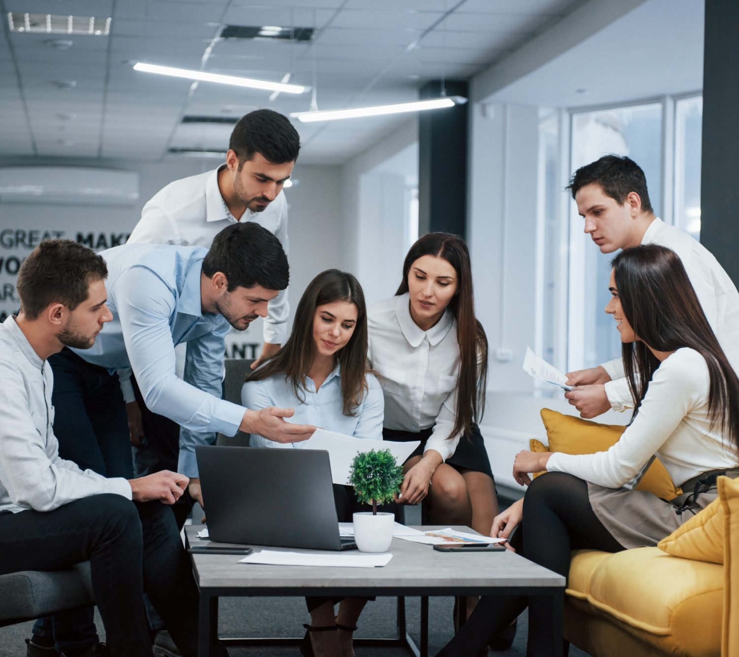 Guy shows document to a girl. Group of young freelancers in the office have conversation and working.